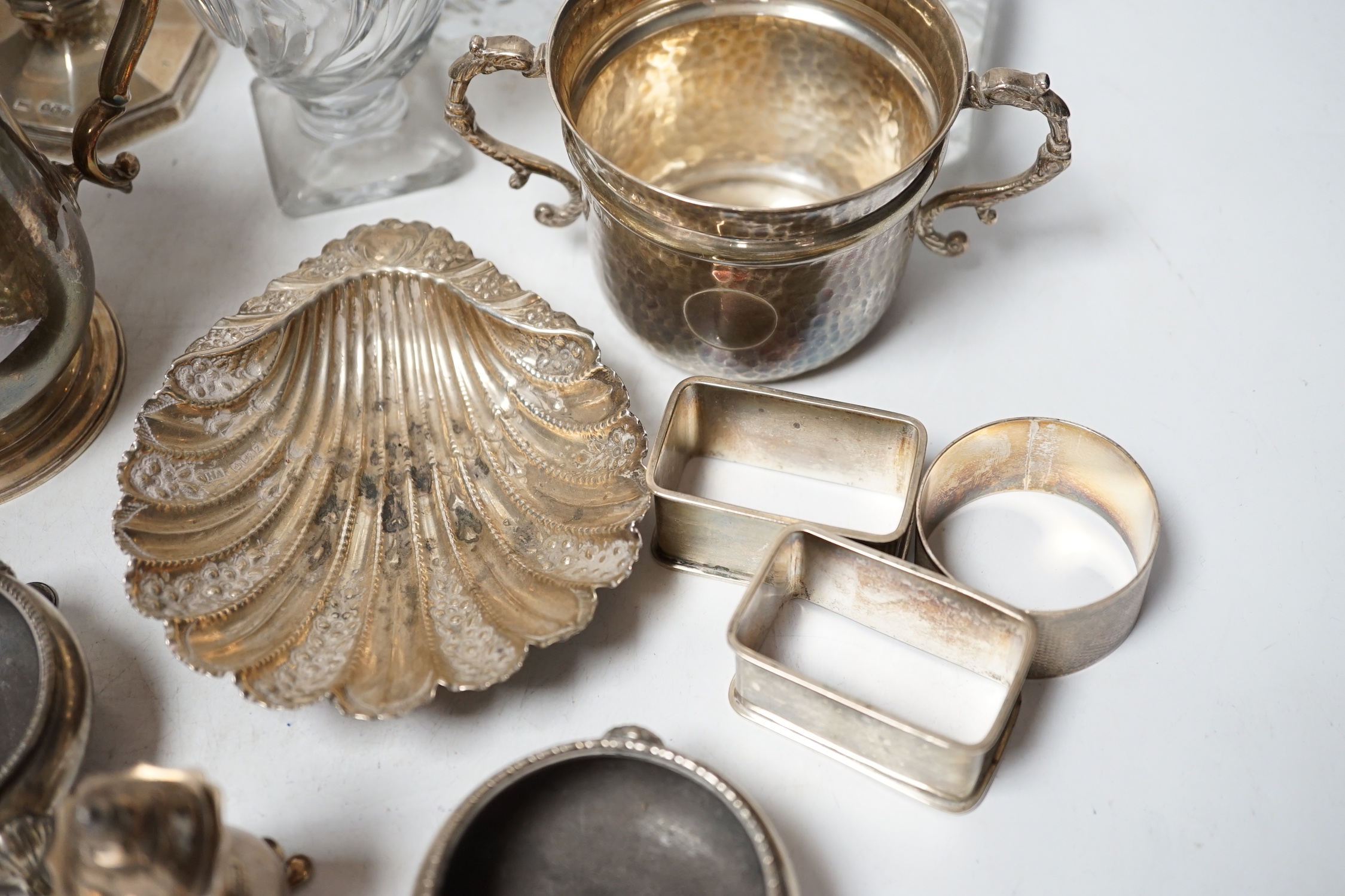 Assorted small silver including a christening mug, a planished porringer, pair of George V sugar casters, butter shell, ashtray, two mounted glass posy vases, four condiments, four napkin rings, a mounted glass cruet bot
